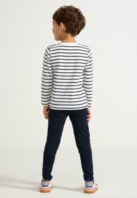 Stribet langærmet skjorte i hvid og marineblå, parret med marineblå bukser. Barnet har casual sko med blå accenter og beige sål.