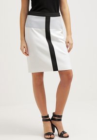 Bílá sukně s přiléhavým střihem, zdobená černým vertikálním pruhm a šedým pasem. Hladká textura; v kombinaci s černými sandály na vysokém podpatku.