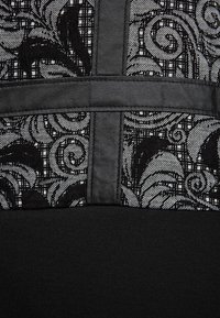 Svart klänning med en texturerad tyg med intrikata blomster mönster i grått och vitt, kontrasterad av en slät svart panel.