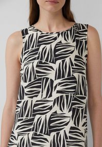 Débardeur texturé au motif de feuilles noir et blanc. Encolure ronde et tissu doux. Le design semble décontracté et léger.