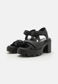 Sorte hælede sandaler med brede stropper, tekstureret overdel og chunky sål. Har en let hævning ved hælen og en justerbar strop.
