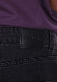 Crne traperice od denima imaju kožni označivač "Dropsize" na struku, s vidljivim šavovima i glatkom teksturom.