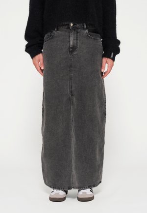 Gonna di jeans maxi nera, con taglio dritto, tasche anteriori e leggera texture sfumata. Indossata con sneakers grigie.