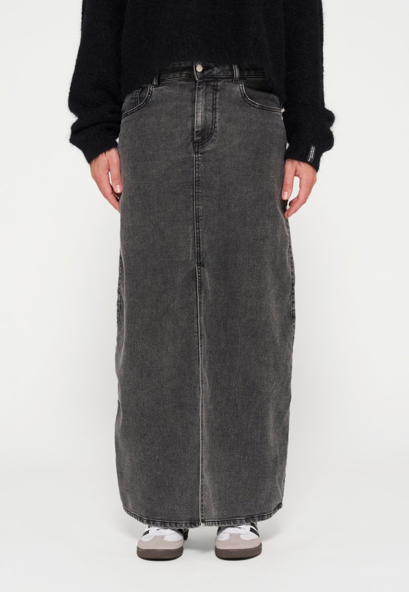 Falda denim maxi en negro, con corte recto, bolsillos delanteros y una sutil textura desgastada. Usada con zapatillas grises.
