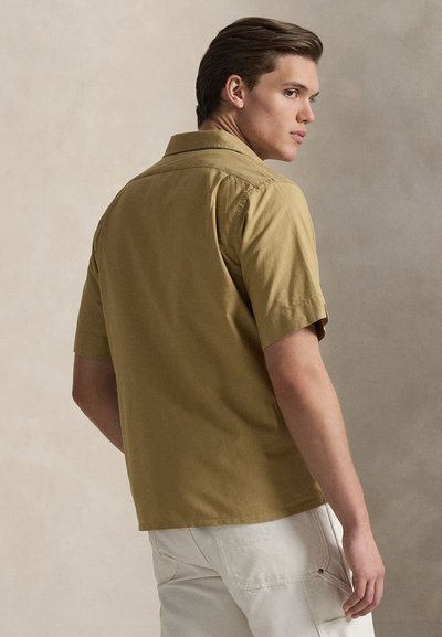 Κοντομάνικο πουκάμισο από βαμβάκι ελιάς, με κλασικό γιακά και άνετη εφαρμογή. Η πίσω όψη αποκαλύπτει λεία υφή και καθαρές γραμμές.