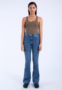 Top de tirantes marrón con textura, combinado con pantalones vaqueros acampanados de cintura alta en azul. La tela parece suave, el denim tiene un lavado clásico, con detalles de botón y bolsillos.