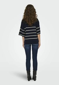 Marinrandig topp med vida ärmar, kombinerad med mörka jeans och svarta ankelstövlar. Slät textur med horisontella krämfärgade ränder.