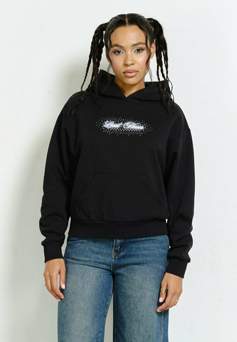 Czarna bluza z kapturem z przednią kieszenią, z białym wzorem tekstowym i akcentami w kropki. W połączeniu z niebieskimi dżinsami, które prezentują swobodny krój.