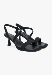Zwarte hoge hak sandalen met een vierkante neus, gemaakt van soepel leder. Kenmerken zijn gekruiste banden en een taps toelopende hak voor ondersteuning.