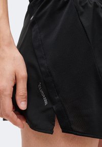 Αριστερό χέρι δίπλα σε μαύρα αθλητικά σορτς με διαπνέον υλικό και το κείμενο «climacool» στη χαμηλότερη πλαϊνή ραφή.