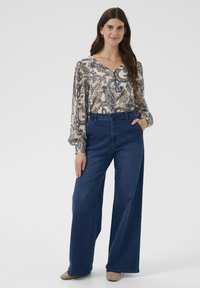 Lahka kremasta bluza s temno modrim paisley vzorcem, kombinirana z visokim pasom širokih temno modrih kavbojk. Mehka tkanina, rahla tekstura in žepi.