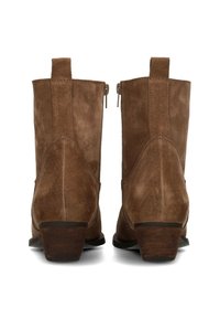 Botines de ante marrón con tacón apilado, que cuentan con cremalleras laterales y una lengüeta en la parte posterior para poner y quitar fácilmente. Textura suave, diseño clásico.