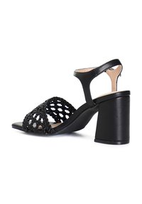 Zapato de sandalia negra con parte superior trenzada y áreas abiertas, correa ajustable en el tobillo y tacón sólido. Textura suave y diseño minimalista.