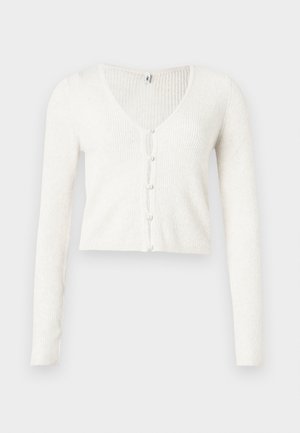Cardigan blanc côtelé avec un col en V, présentant un ourlet court et six boutons nacrés sur le devant. Manches longues et ajustées.