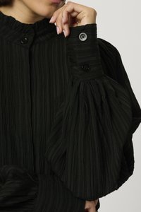 Blusa nera con texture, colletto alto, chiusure a bottoni sulle maniche e maniche voluminose a palloncino. Il tessuto presenta un design arricciato.
