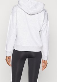 Grå huvtröja med huva, med avslappnad passform och ribbade ärmslut, i kombination med svarta leggings som har vita sidostreck.