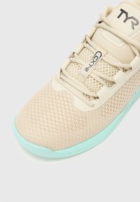 Beżowe siatkowe sneakersy z miętową podeszwą, posiadające teksturowaną cholewkę, detal związany ze sznurowaniem oraz wyraźne logo na języku.