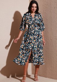 Floral print dress with navy background, short puff sleeves, cinched waist, and side slit. Made from lightweight fabric with a smooth texture.