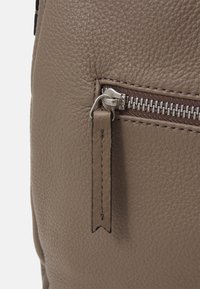 Pelle marrone testurizzata con una tasca con zip. La cerniera è dotata di un tirante metallico e di cuciture a contrasto lungo i bordi.