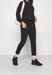 Svart quiltad sweatshirt med långa ärmar och rundad halsringning, kombinerad med matchande tapered byxor och svarta sneakers; har en vit väska.