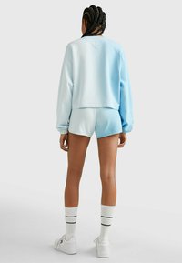 Sudadera azul claro y conjunto de pantalones cortos a juego. La sudadera tiene un corte relajado; los shorts tienen una banda elástica en la cintura. Calcetines blancos con rayas en navy.