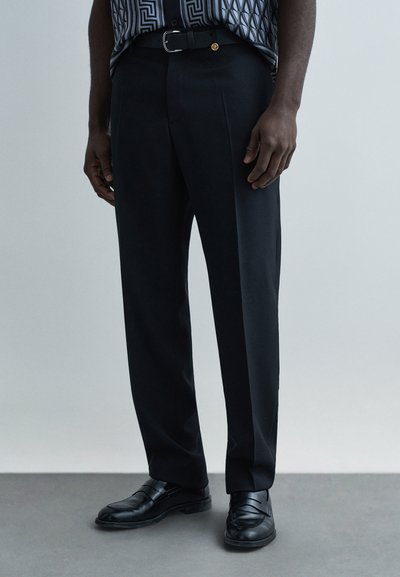Pantalon noir ajusté avec un devant plat, présentant une coupe slim et un pli net. Assorti à des chaussures de ville noires et une ceinture assortie.