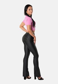 Musta, istuva liehuva housut sileällä pinnalla ja hienovaraisilla ompeluilla, yhdistettynä lyhyeen vaaleanpunaiseen toppiin ja mustiin korkokenkiin.