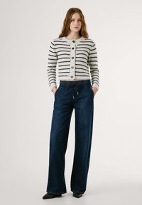 Striped knitted cardigan in cream and navy, featuring a round neckline, button closure, and wide-leg dark blue pants with an elastic waistband.