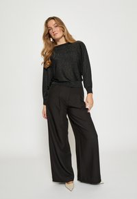 Black, metallic knit sweater with long sleeves paired with high-waisted black wide-leg trousers. Pointed beige heels complete the outfit.