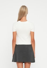Top alb cu mâneci scurte și decolteu rotund, purtat cu o fustă alb-negru cu carouri, având un design evazat și o textură subtilă.