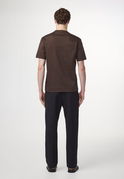 Chemise marron à manches courtes avec un col rond, associée à un pantalon noir à rayures. Le matériau semble lisse et structuré.
