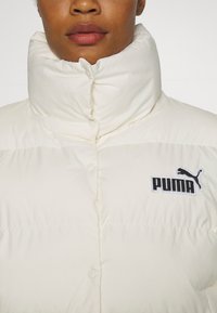 Puffy white jacket with a high collar, featuring a button closure and a black Puma logo patch on the left chest area. Smooth, insulated fabric.