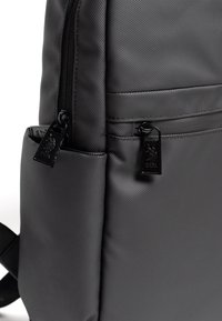 Czarny plecak wykonany z teksturowanego materiału, wyposażony w dwa zamki błyskawiczne z oznakowanymi suwakami, boczną kieszeń oraz wyściełane paski na ramiona.