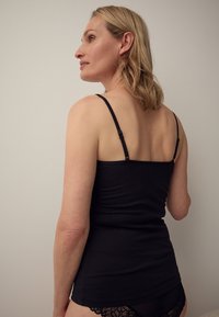 Camiseta negra con tirantes finos ajustables, diseño ajustado, tela suave y espalda sin costuras, combinada con ropa interior negra de encaje.