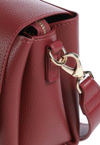 Borsa in pelle bordeaux con finitura testurizzata, dotata di una chiusura a moschettone in metallo dorato e un dettaglio di attacco della tracolla.
