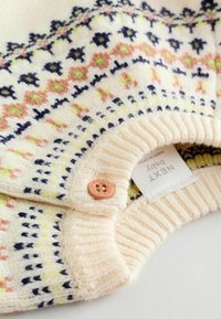 Creme strikket sweater med farverige blomster mønstre i pink, grøn og marineblå. Ribbet manchetter og en ferskenfarvet knap ved kraven.
