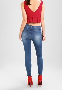 Jeans blu aderenti con vita media e un leggero sbiadimento, abbinati a un top peplum rosso e stivaletti con tacco rossi.