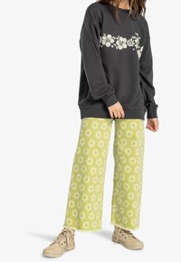 Sudadera gris con un diseño floral en el pecho, combinada con pantalones de pierna ancha en un verde claro con un patrón de sol, y zapatos beige.