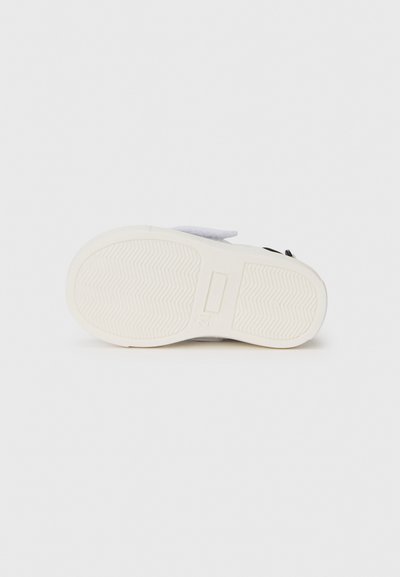 White rubber sneaker sole with a textured herringbone pattern. Features a grey fabric upper with a hook-and-loop strap for fastening.