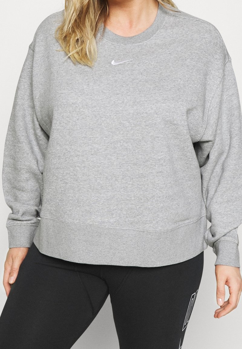 Grå sweatshirt i mjukt tyg, med rund halsringning, sänkt axelsöm och en liten vit logotyp på bröstet.