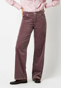 Corduroy pants in deep mauve, featuring wide legs, five pockets, and subtle texture. Paired with dark, glossy shoes and a pink striped shirt.