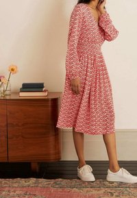 Vestido de estampado floral rojo con mangas largas abullonadas, cintura fruncida y falda hasta la rodilla, combinado con zapatillas blancas.