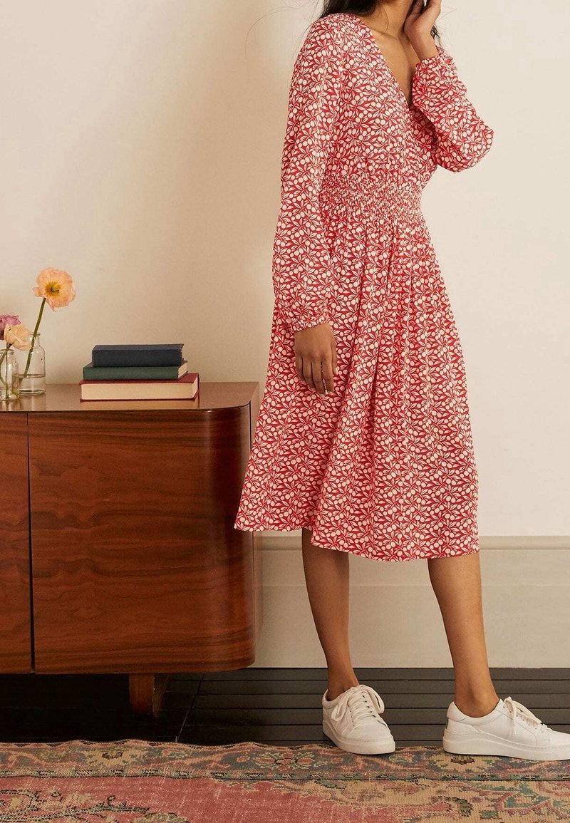 Vestido de estampado floral rojo con mangas largas abullonadas, cintura fruncida y falda hasta la rodilla, combinado con zapatillas blancas.