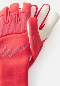 Gants de sport rouges en tissu texturé, offrant un ajustement serré et des accents blancs. Comprend une étiquette "Dynamic Fit" sur le côté.