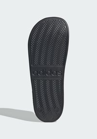 Crna gumena potplat tenisice s uzorkom riblje kosti. Sadrži istaknuto "adidas" brendiranje u srednjem dijelu. Glatka tekstura općenito.