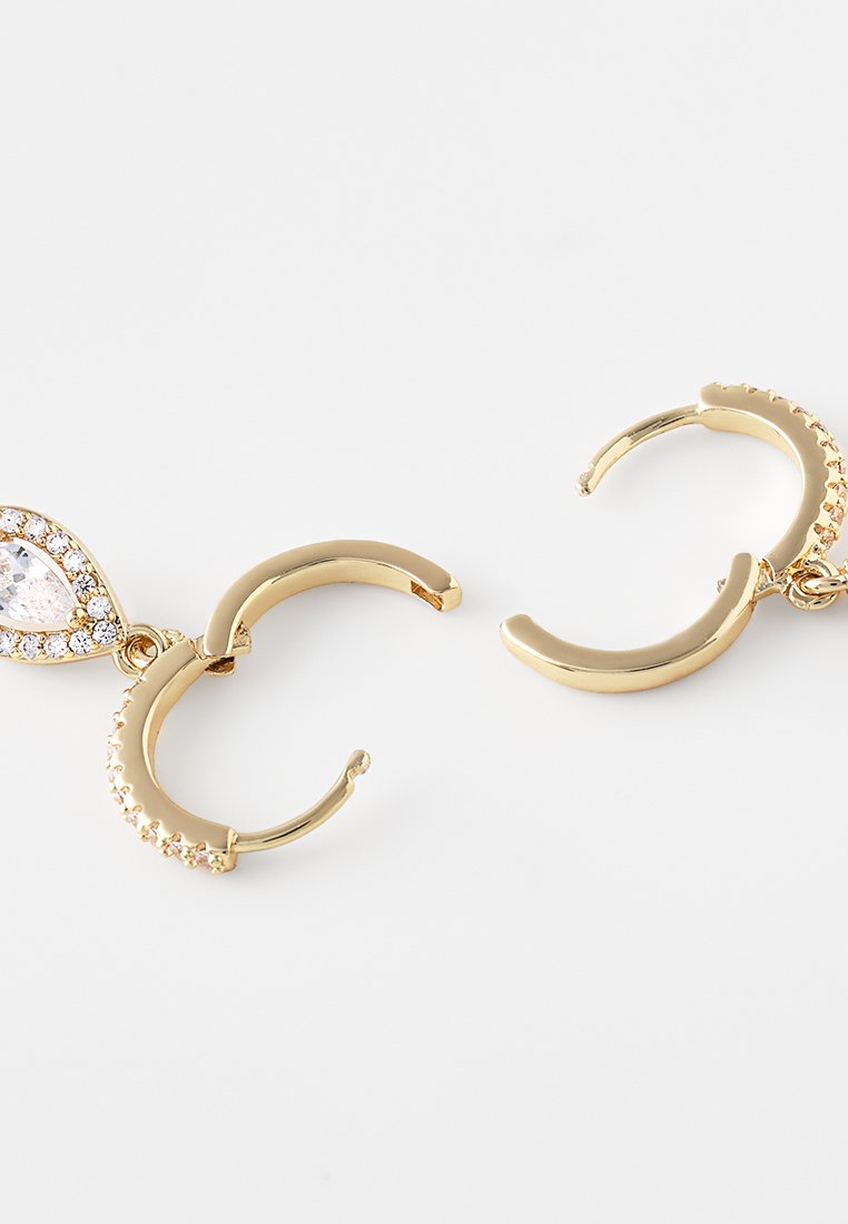 Boucles d'oreilles en ton or en forme de créole, mettant en avant un cristal en forme de goutte d'eau entouré de petits strass transparents et offrant une finition lisse et polie.