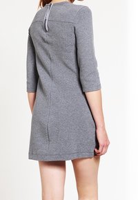 Grå, knälång klänning i mjukt tyg, med 3/4 ärmar, rundad halsringning och synlig dragkedja i ryggen.