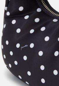 Czarna torba materiałowa w duże białe kropki, z złotym zamkiem błyskawicznym i małym detalem z logo. Gładka tekstura i zakrzywiony kształt.