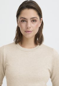 Haut en maille côtelée beige avec un col rond, des manches courtes et une texture lisse. Design simple et ajusté sans ornements.