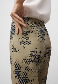 Beige broek met een patroon van zwarte en blauwe stippen, met een gladde textuur en een achterzakdetail. Casual ontwerp.